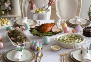 a beautifully decorated Easter table with a person serving on to a plate and serving dishes of deviled eggs, asparagus, and roasted turkey breast and herb crusted rack of lamb, creamy spinach dip with raw vegetables, and chocolate cake.